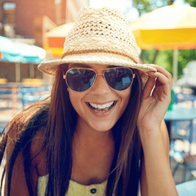 Young woman in fedora and sunglasses smiling