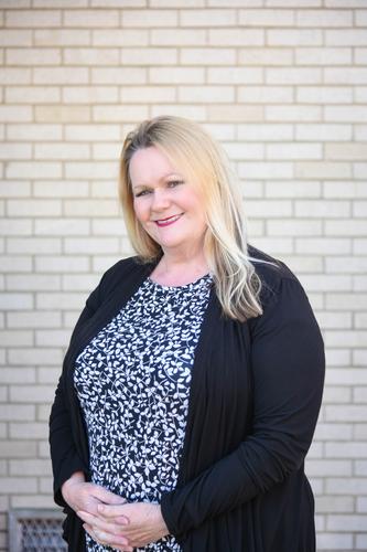 Woman with straight teeth smiling in front of white wall outside after orthodontic treatment
