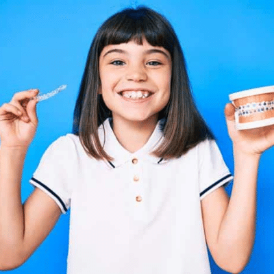 Early orthodontic treatment 9 Little girl holding up invisalign aligners in one hand and plastic teeth in the other, representing early orthodontic treatment