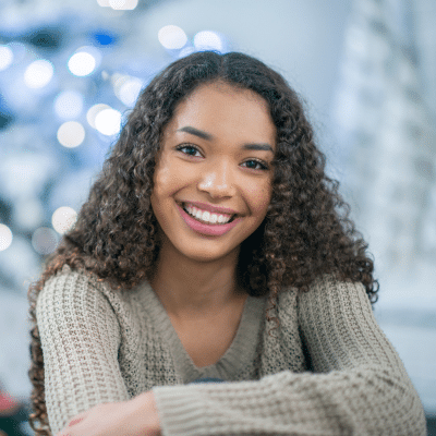 Orthodontic treatment: ensuring your teen's smile lasts a lifetime 7 Teenage girl smiling, wearing green on a sweater with a bluish background, representing teen orthodontic treatment