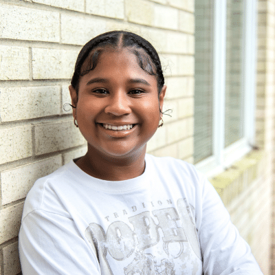 Female patient leaning against a brick wall, smiling and posing, representing representing braces vs aligners