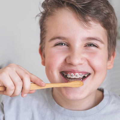 Smiling child with braces brushing their teeth, demonstrating tips for brushing and flossing with braces recommended by maddux orthodontics in virginia beach, va