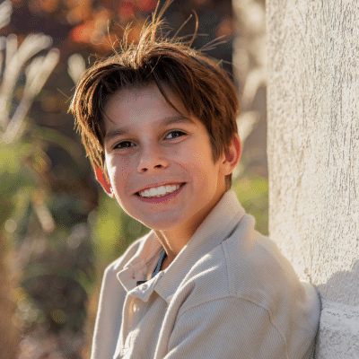 Smiling boy leaning against a wall outside at maddux orthodontics, representing how braces have evolved over time